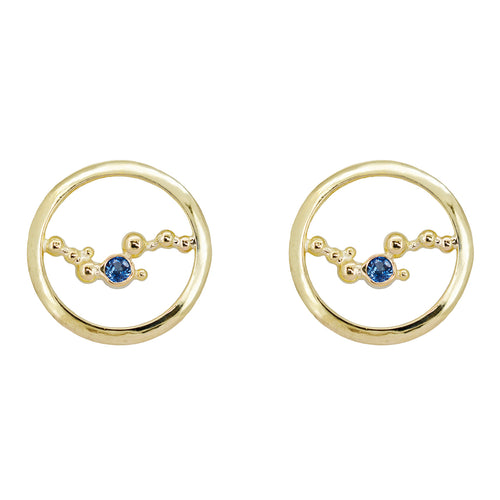 These stud earrings are handcrafted with solid 18K yellow gold, & a single 3mm Ceylon blue sapphire embraced in the middle of an abstract array of gold granulation. Against a white background. 