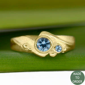 This ring, Rising Tide, embodies the motion and the balance of the sea. The ocean-blue Montana Sapphires are encircled by wave formations sculpted in 18K yellow gold. Around the gemstone, the metal is hand-textured creating a sparkling sand-like finish along with sea foam bubbles that dance across the wave. The band is finished with a high polish.