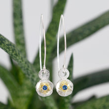 Load image into Gallery viewer, The Beacon of Hope dangles depicts a single glistening forget-me-not flower, symbolizing light, hope, and enduring love. These earrings is handcrafted using tarnish resistant sterling silver, and a Ceylon blue sapphire set in 18K yellow gold. Chloe Leigh Designs: Handcrafted Fine Jewelry