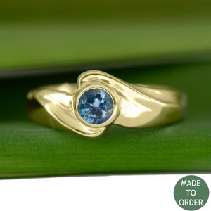 This ring, Timeless, embodies the elegance and harmony of the sea. This is a timeless solitaire ring with a unique flare. The ocean blue Montana sapphire is encircled by a graceful wave in 18K Yellow Gold. The band is finished with a high polish.
