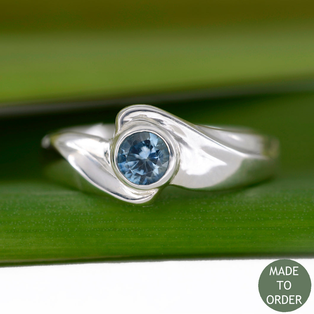 This ring, Timeless, embodies the elegance and harmony of the sea. This is a timeless solitaire ring with a unique flare. The ocean blue Montana sapphire is encircled by a graceful wave in Silver. The band is finished with a high polish.